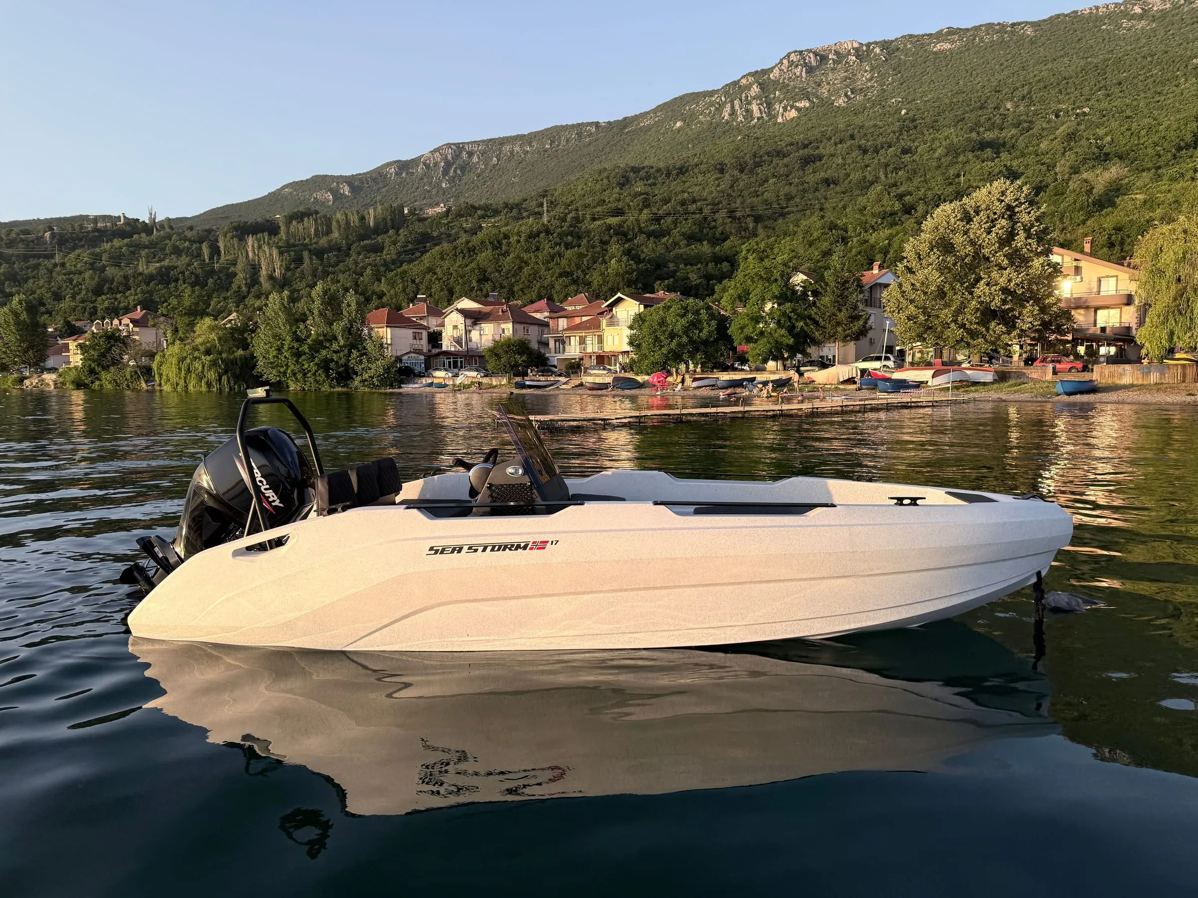SeaStorm 17 im Abendlicht vor einem Bergdorf am See, bereit für Vermietung und Charter